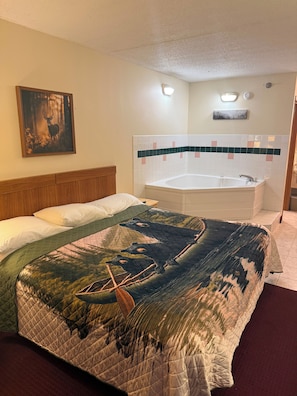 A hotel room with a large bed, a painting of a deer, a bathroom with a bathtub, and a tiled wall. - Ozark Valley Lodge (Branson)