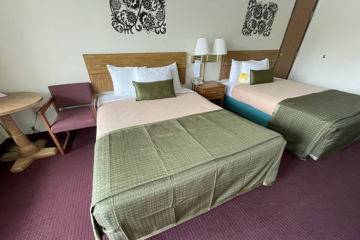 Habitación de hotel con dos camas, cabecero de madera, una mesita, una silla y decoración en la pared.