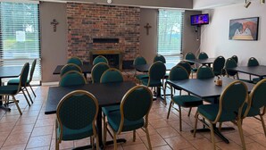 A conference room with a brick fireplace, green upholstered chairs, and a television mounted on the wall. - Ozark Valley Lodge (Branson)