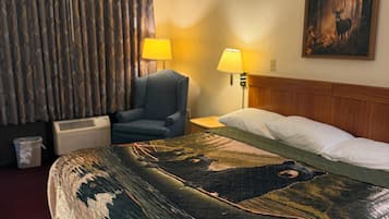 Een hotelkamer met een groot bed, twee bedlampen, een stoel, een schilderij aan de muur en een gordijn.