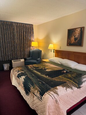 Ein Hotelzimmer mit einem großen Bett, zwei Nachttischlampen, einem Sessel, einem Gemälde an der Wand und einem Vorhang.
