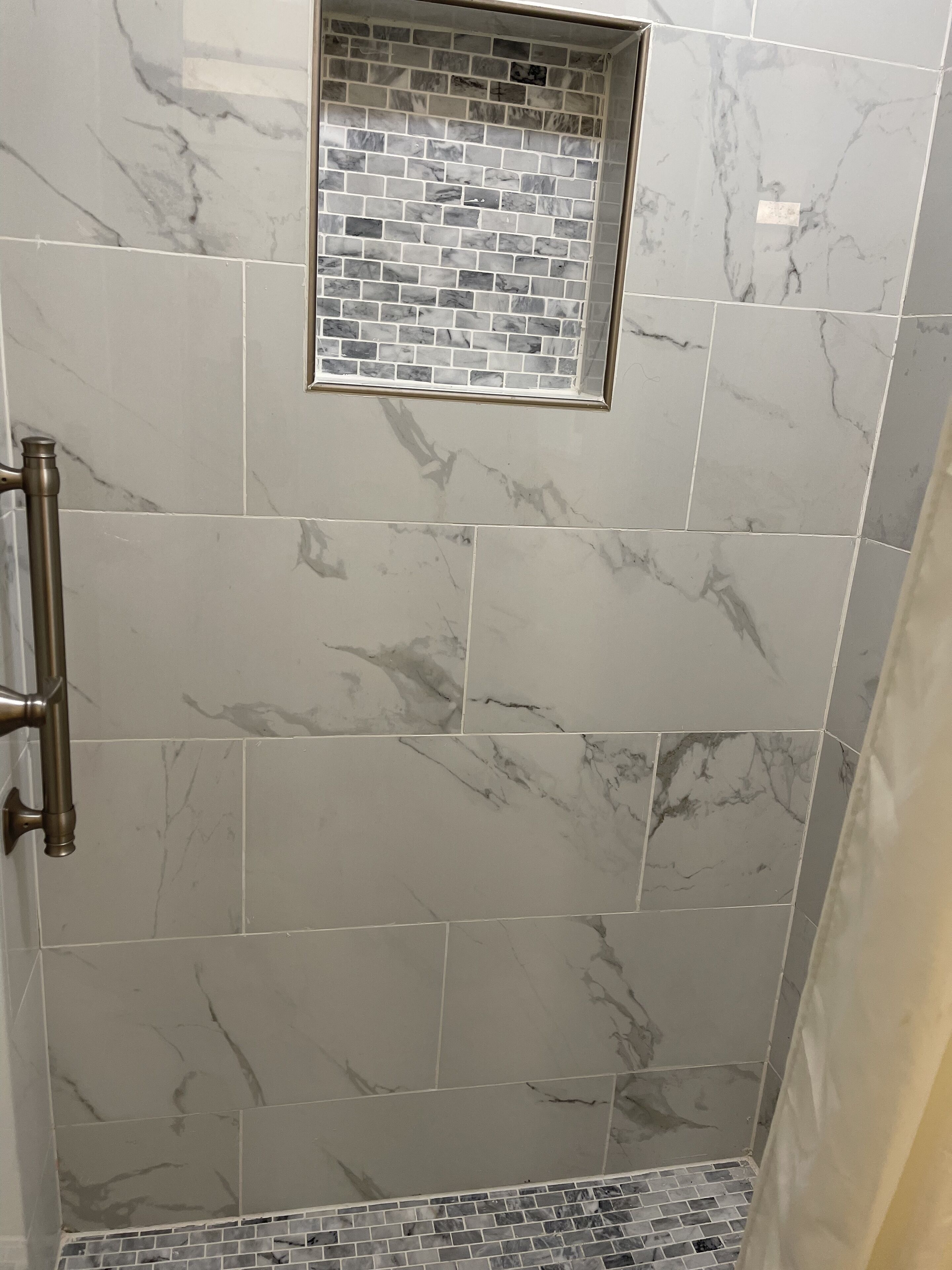 A shower area with large marble tiles and a small mosaic tile accent.