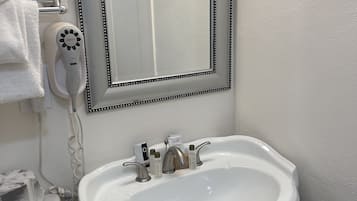 Une salle de bain avec un lavabo blanc, un miroir avec un cadre décoratif, un sèche-cheveux et des articles de toilette.
