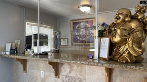 A reception desk with a marble counter, a large golden statue, framed certificates, and a ceiling light. - The Palomar Inn (Pismo Beach)