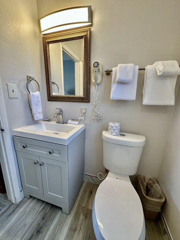 Un baño con lavamanos, tocador, espejo, inodoro y toallero.