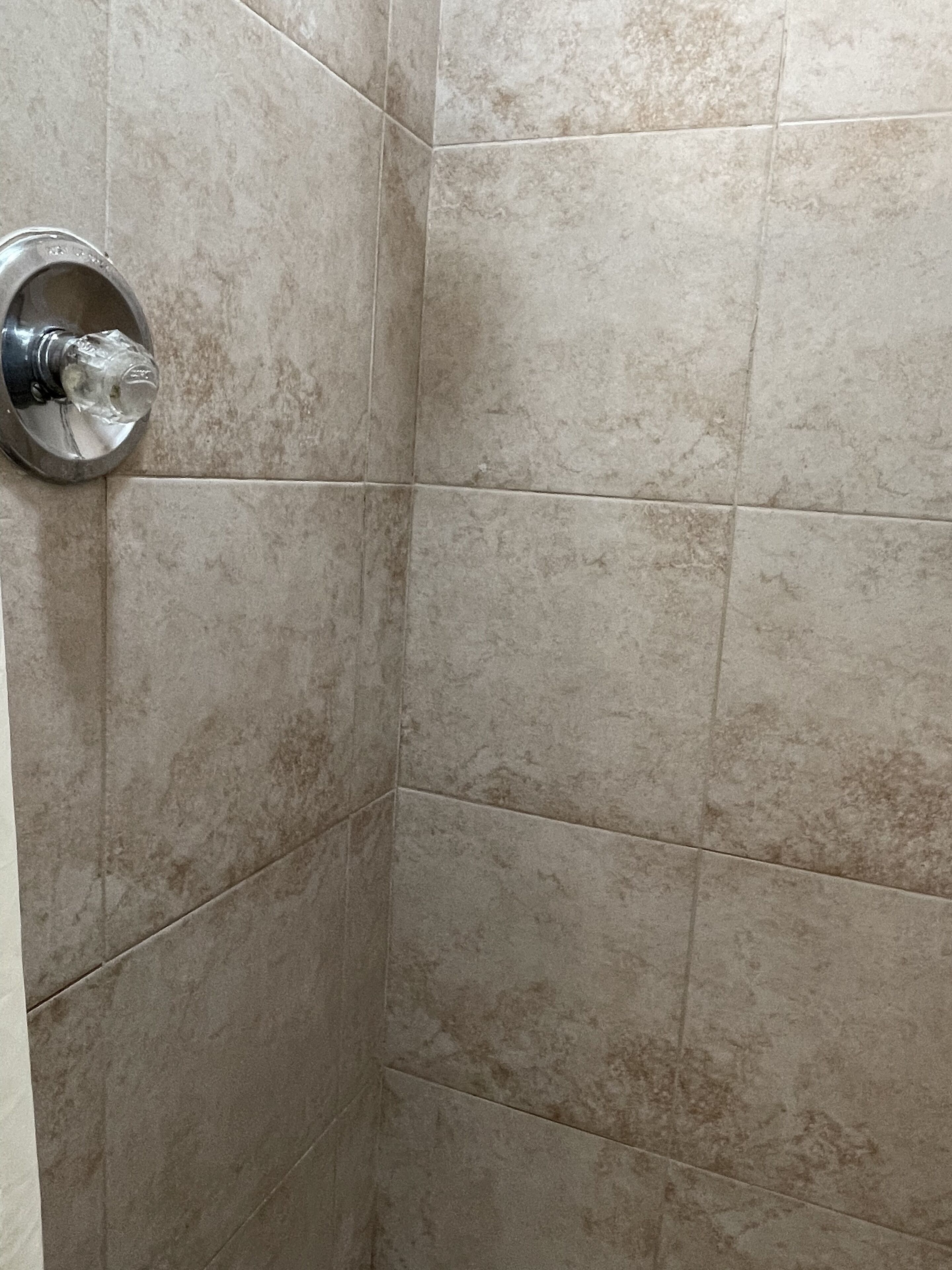 A corner of a bathroom with beige tiles and a chrome faucet.