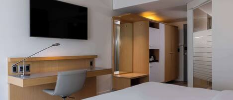 A hotel room with a bed, a desk with a chair, a TV, and a wardrobe.