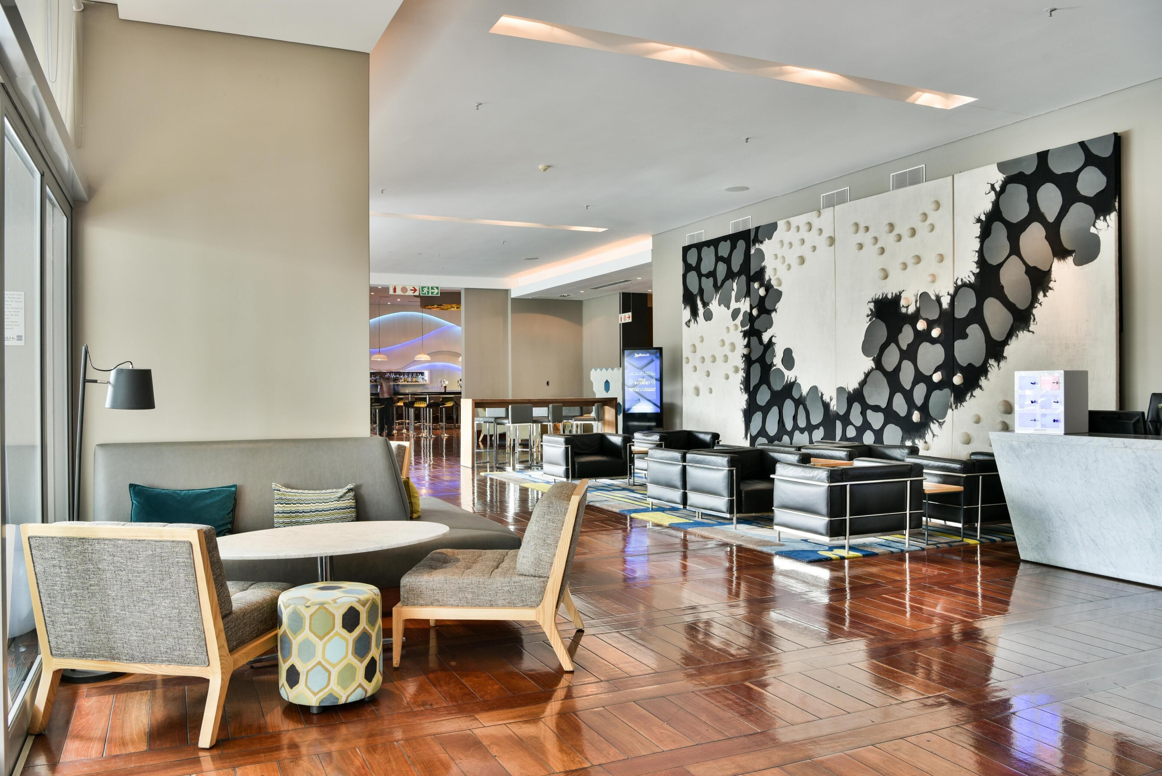 Eine Hotellobby mit Empfangsschalter, Sitzgelegenheiten und einem großen, abstrakten Wandbild.