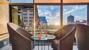 A modern room with a glass table, two grey armchairs, and a city view through large windows.