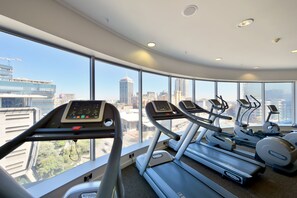A modern gym with treadmills and elliptical machines, large windows offering city views.