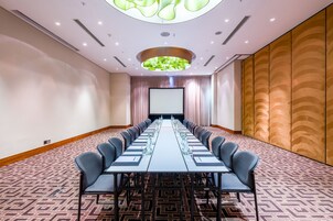 A conference room with a long table, chairs, a projector screen, and a patterned carpet.