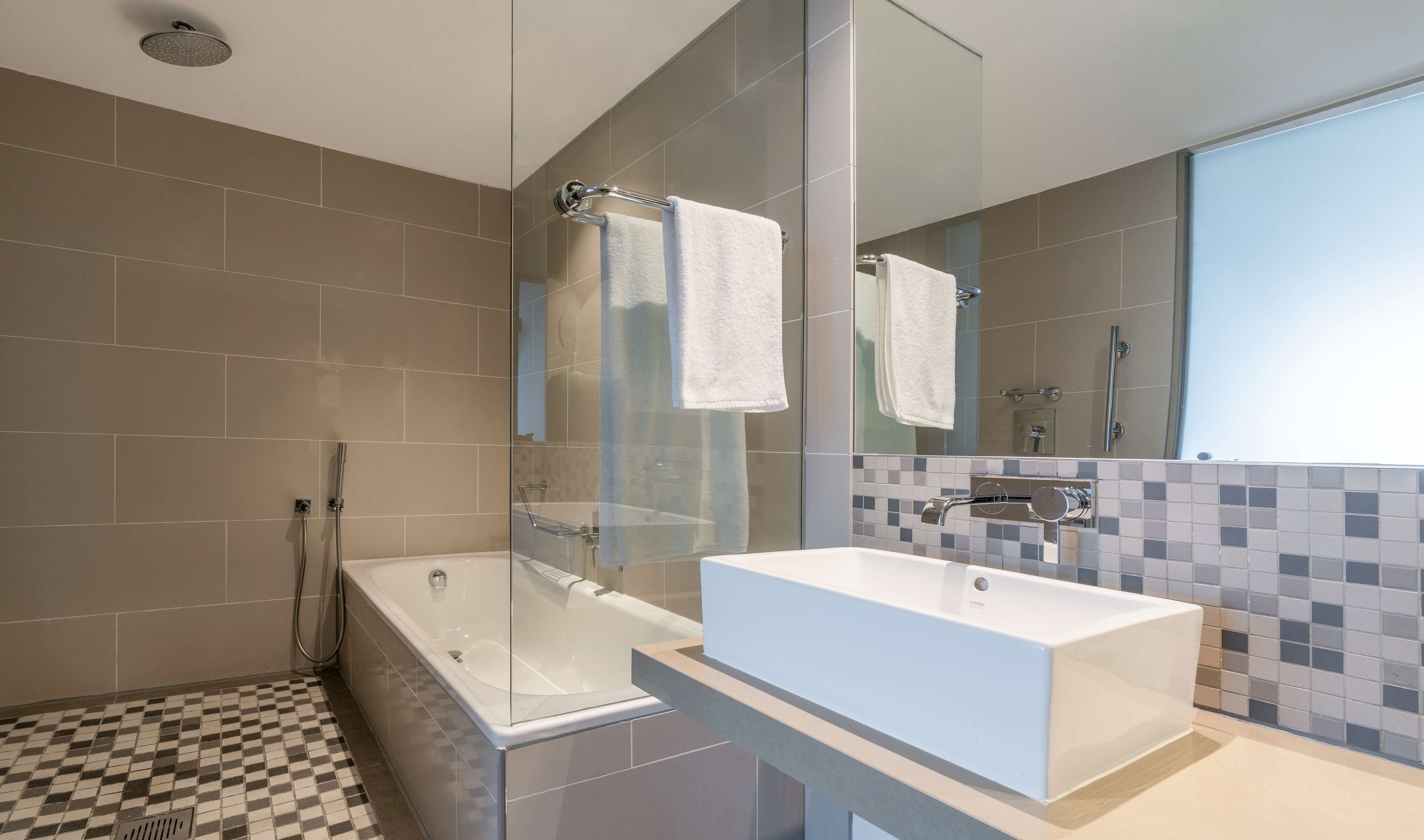A modern bathroom with a glass-enclosed shower, a standalone bathtub, and a large mirror above a tiled vanity.