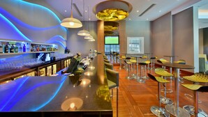 A modern bar area with a long counter, bar stools, and a television screen.