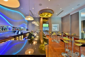 Un espace bar moderne doté d’un long comptoir, de tabourets de bar et d’un écran de télévision.