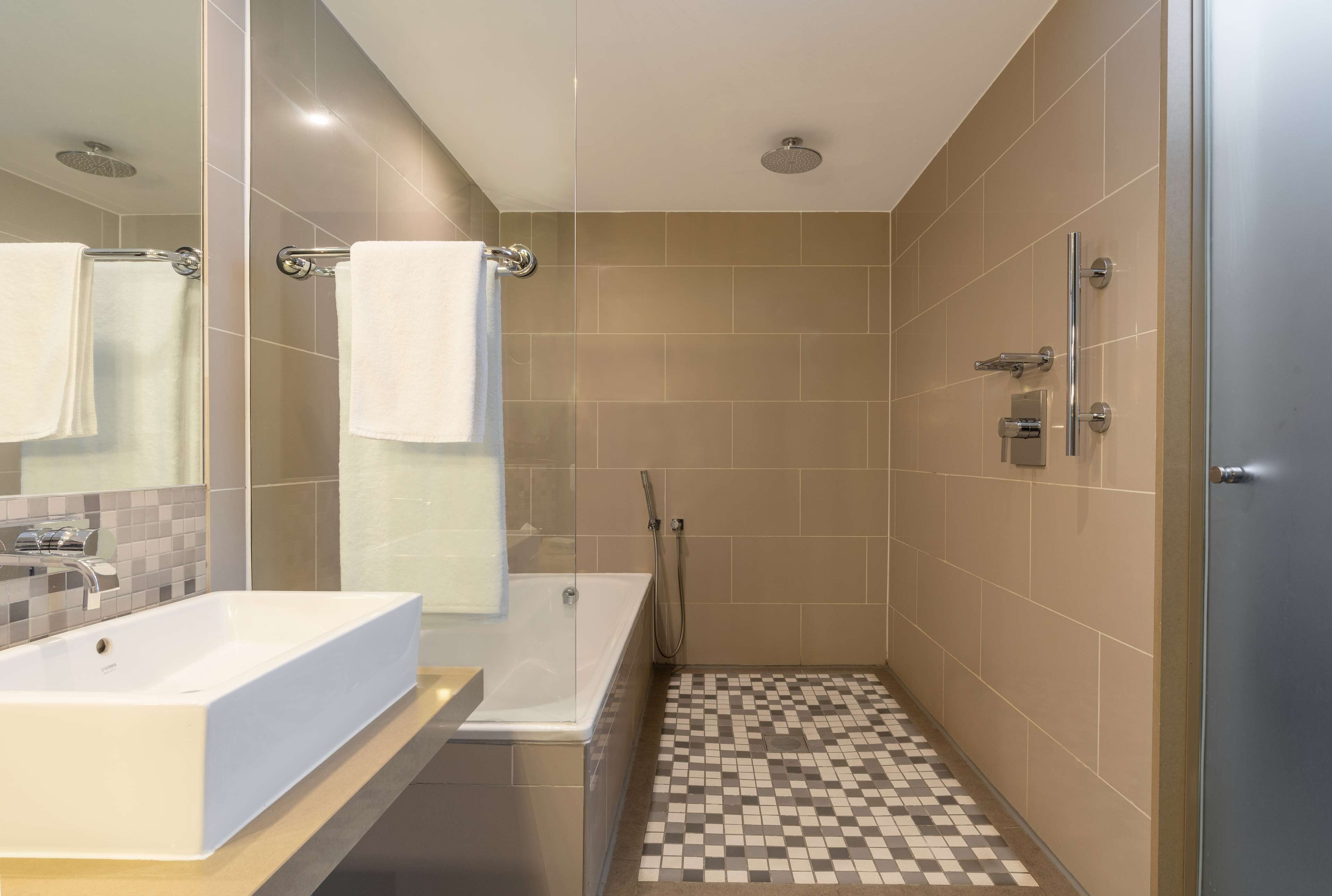 A modern bathroom with a large white sink, a glass-enclosed shower, and a checkered floor.