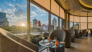 A modern hotel room with a city view, a glass table, and comfortable seating.