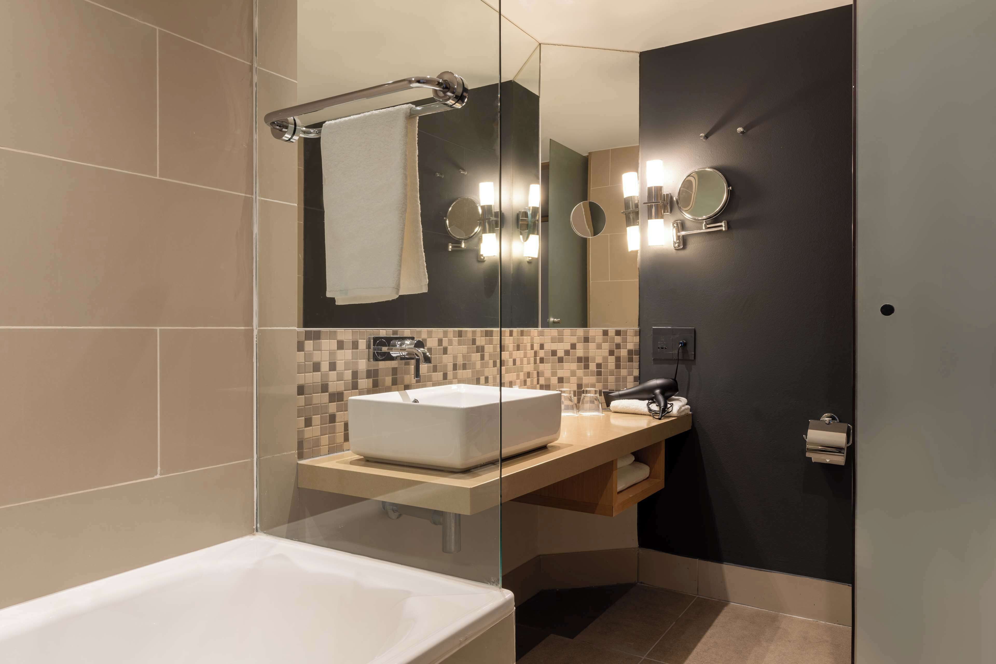 Een moderne badkamer met een wastafel met glazen ombouw, een grote spiegel en een handdoekrek.