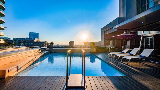 A rooftop pool with sunlit lounge chairs and a clear view of the city skyline.