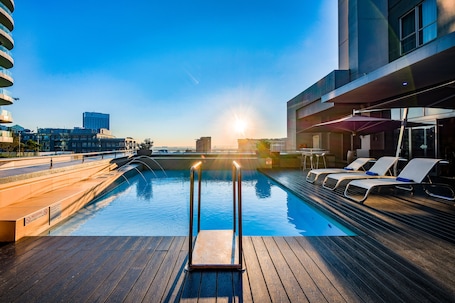Una piscina al aire libre, sombrillas, sillones reclinables de piscina