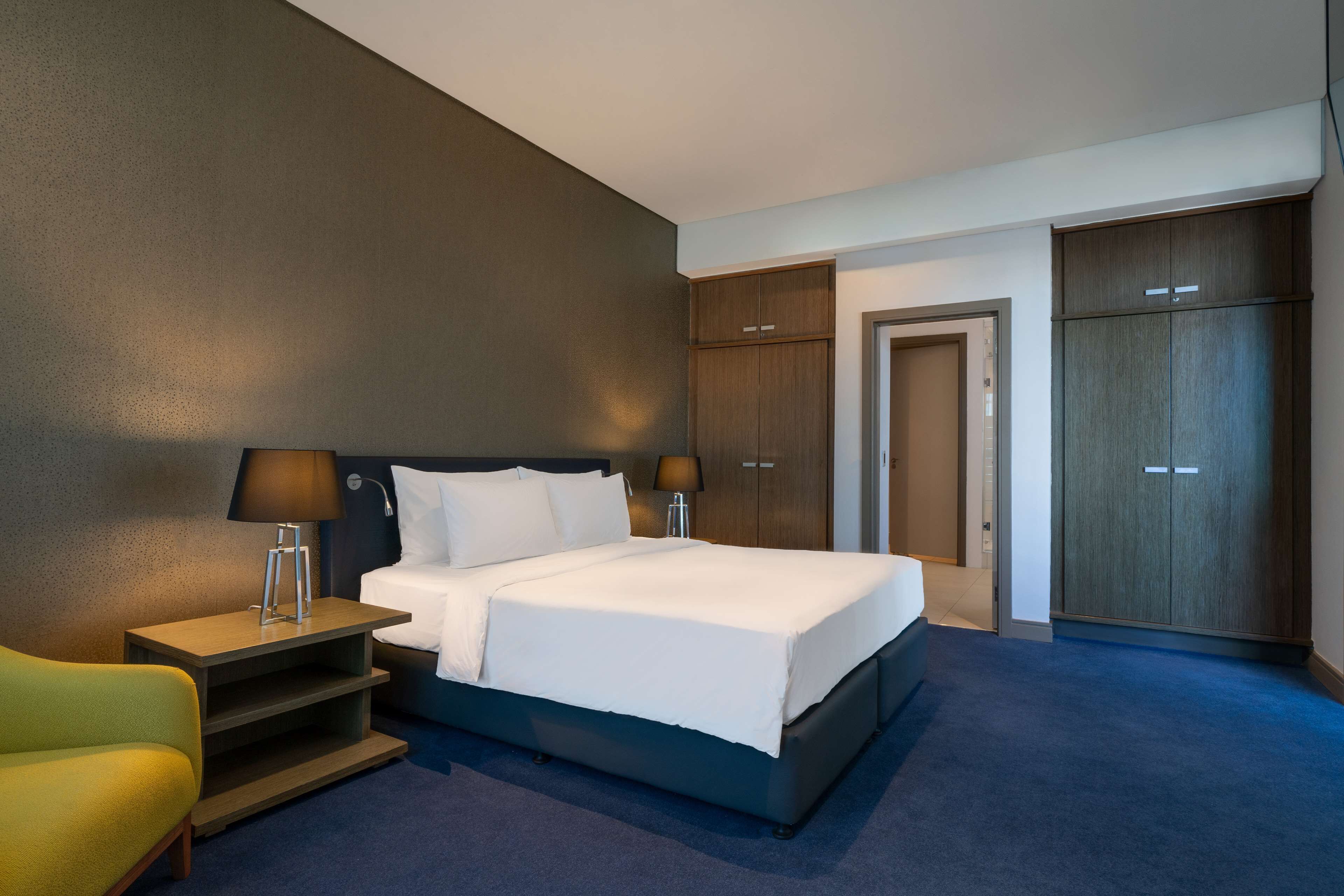 A hotel room with a bed, bedside tables, a chair, and wardrobes.