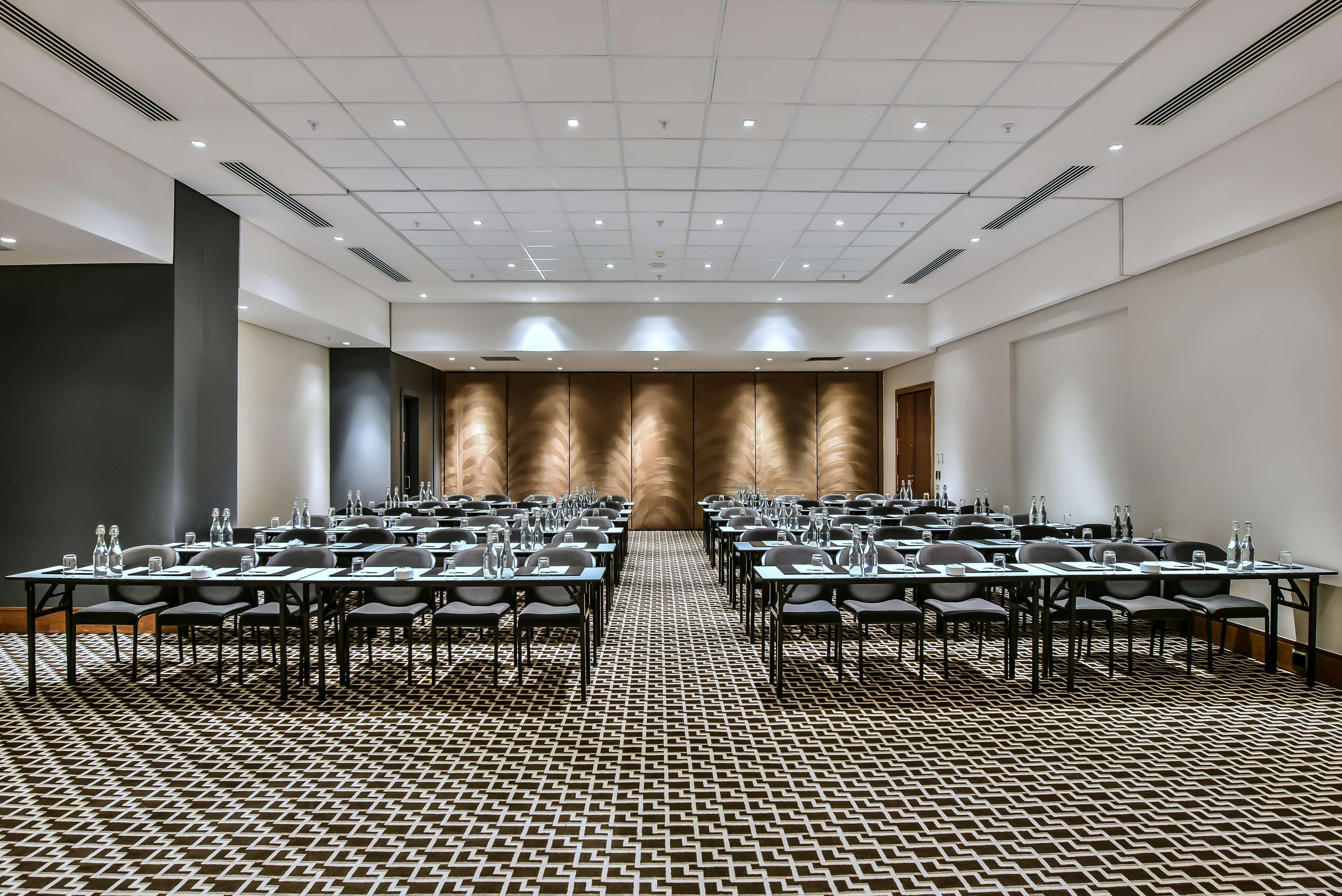 A conference room with a patterned carpet, multiple tables with chairs, and a large wall with a textured design.