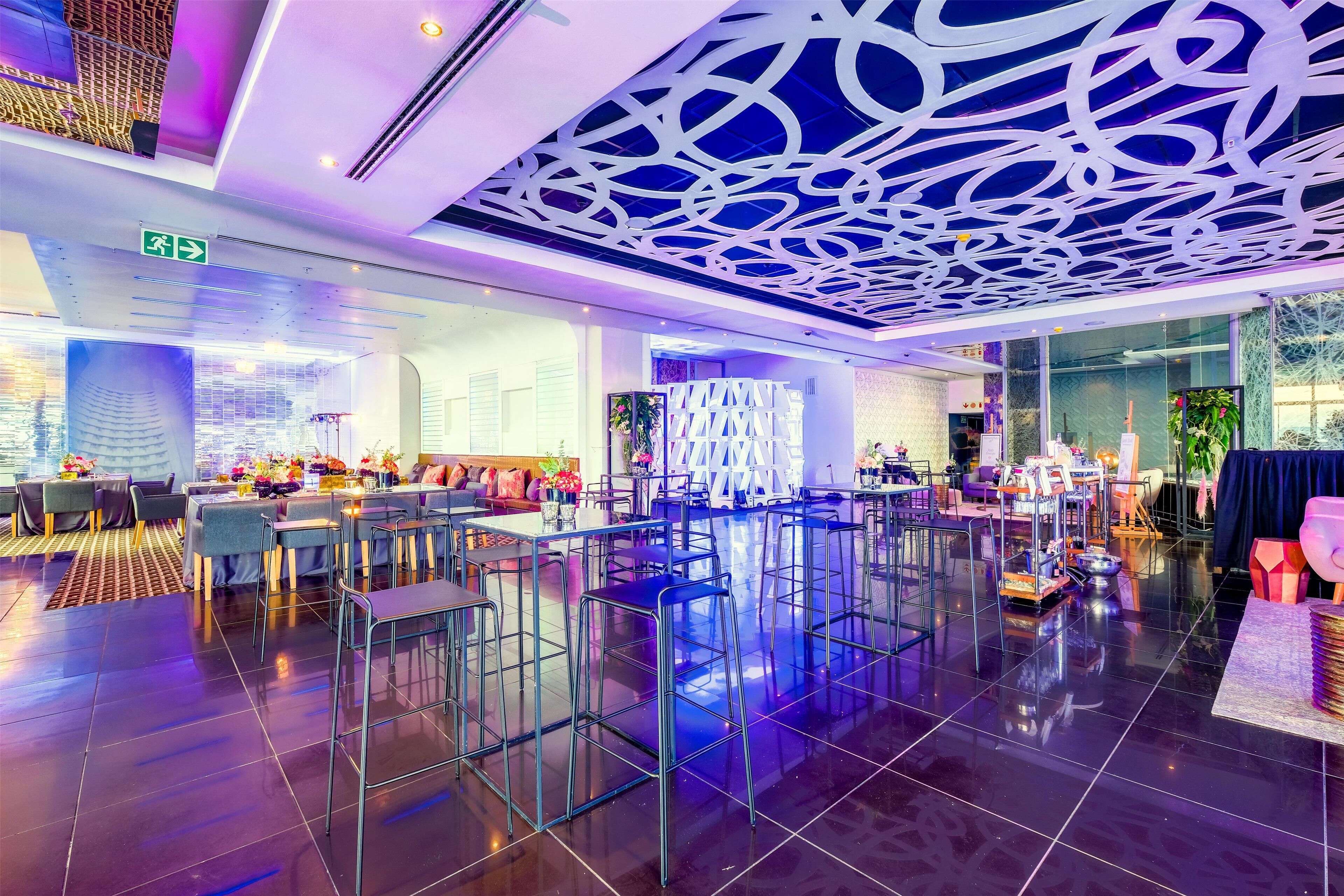 A modern restaurant with high ceilings, a patterned ceiling, and a polished floor.