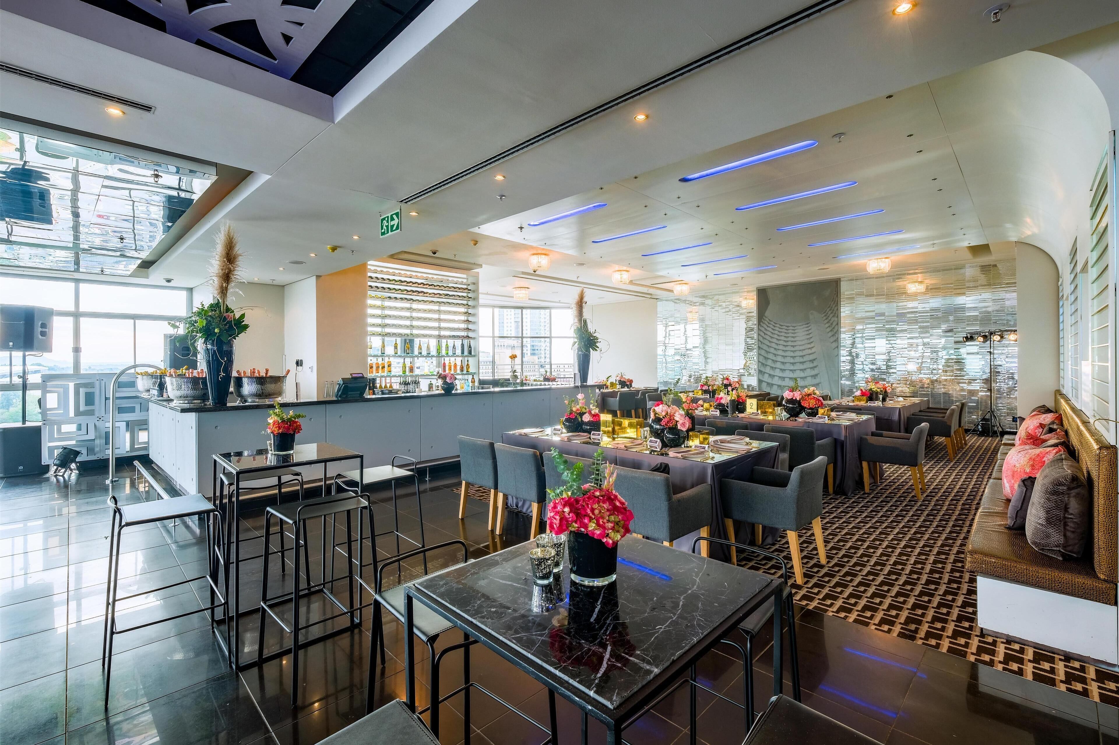 A modern restaurant with a bar area, seating arrangements, and decorative plants.