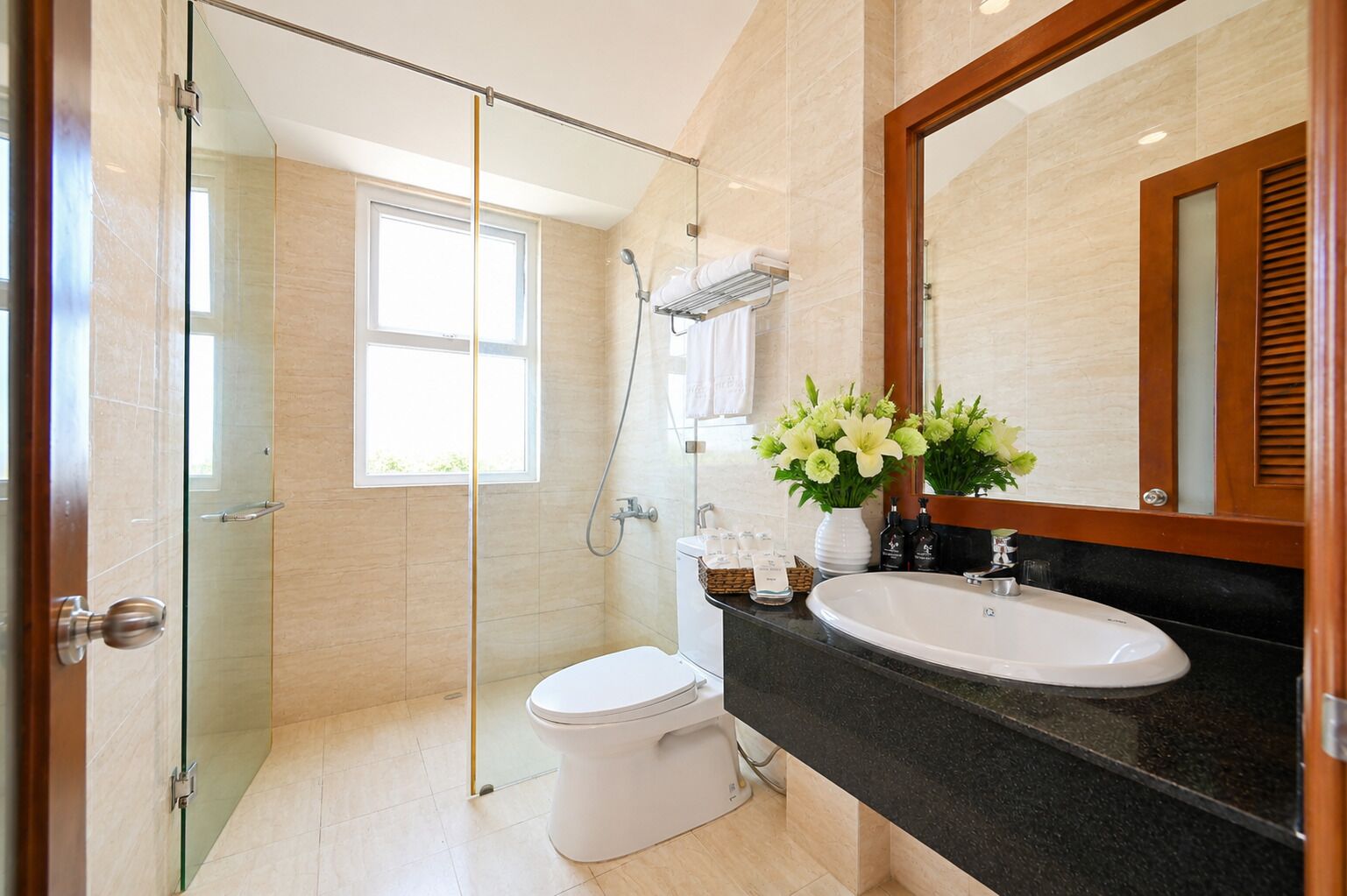 A modern bathroom with a glass shower enclosure, a white toilet, a sink with a black countertop, and a mirror with a wooden frame.