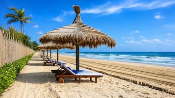 A beach with thatched umbrellas and sun loungers along the shore.