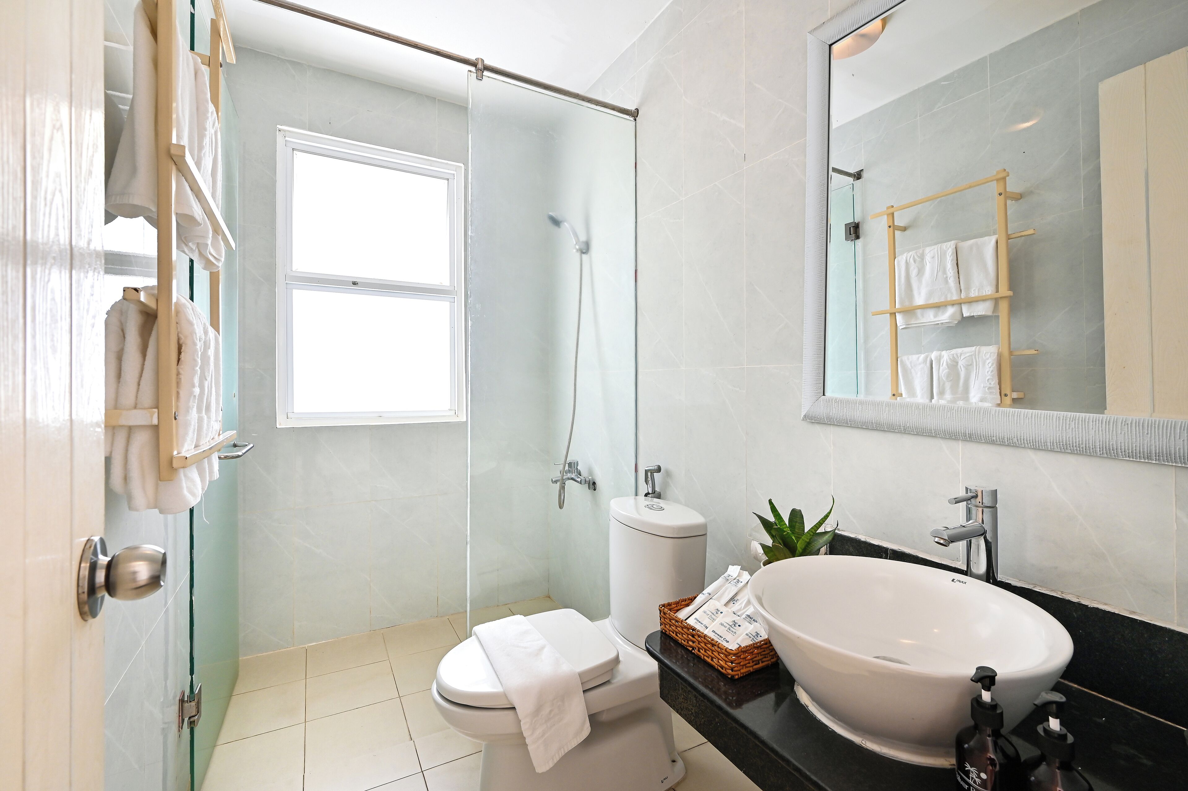 Une salle de bain moderne dotée d’une douche à parois de verre, de toilettes blanches, d’un lavabo avec un grand bac et d’un miroir avec un porte-serviettes.