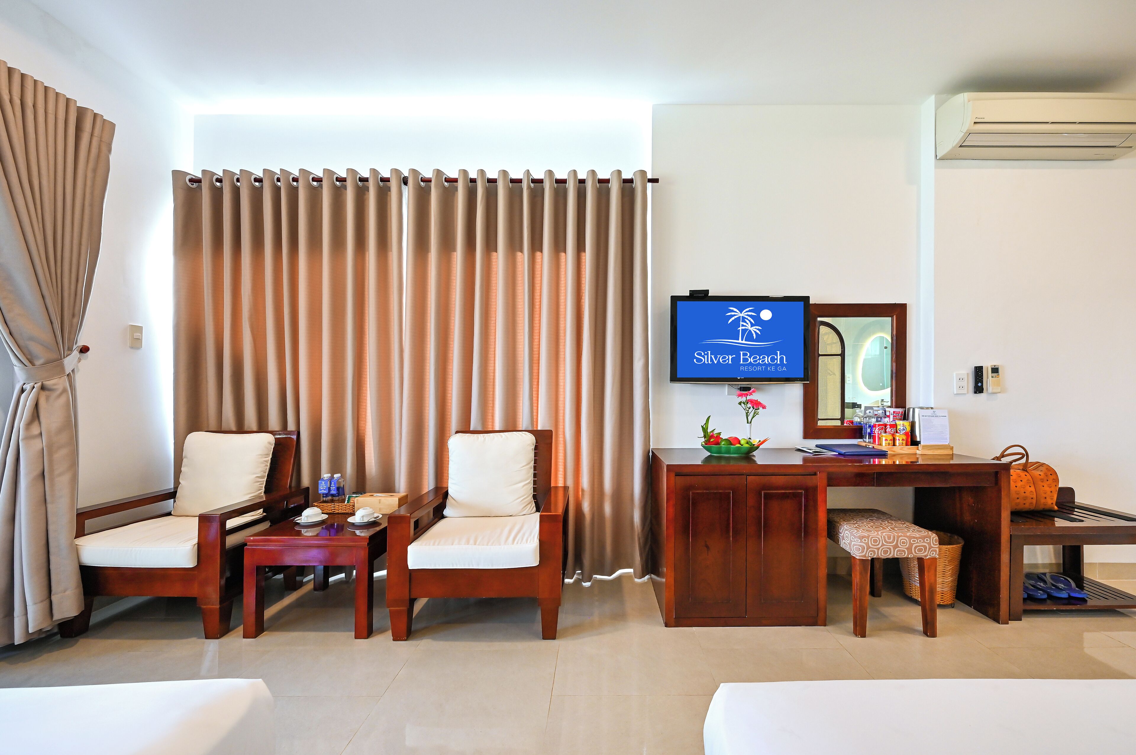 Quarto de hotel com televisão, duas cadeiras, escrivaninha com computador e cama.
