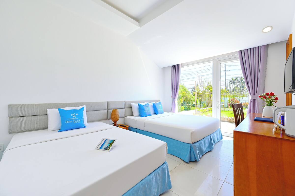 A hotel room with two beds, a wooden desk, a television, and a view of the outdoors.