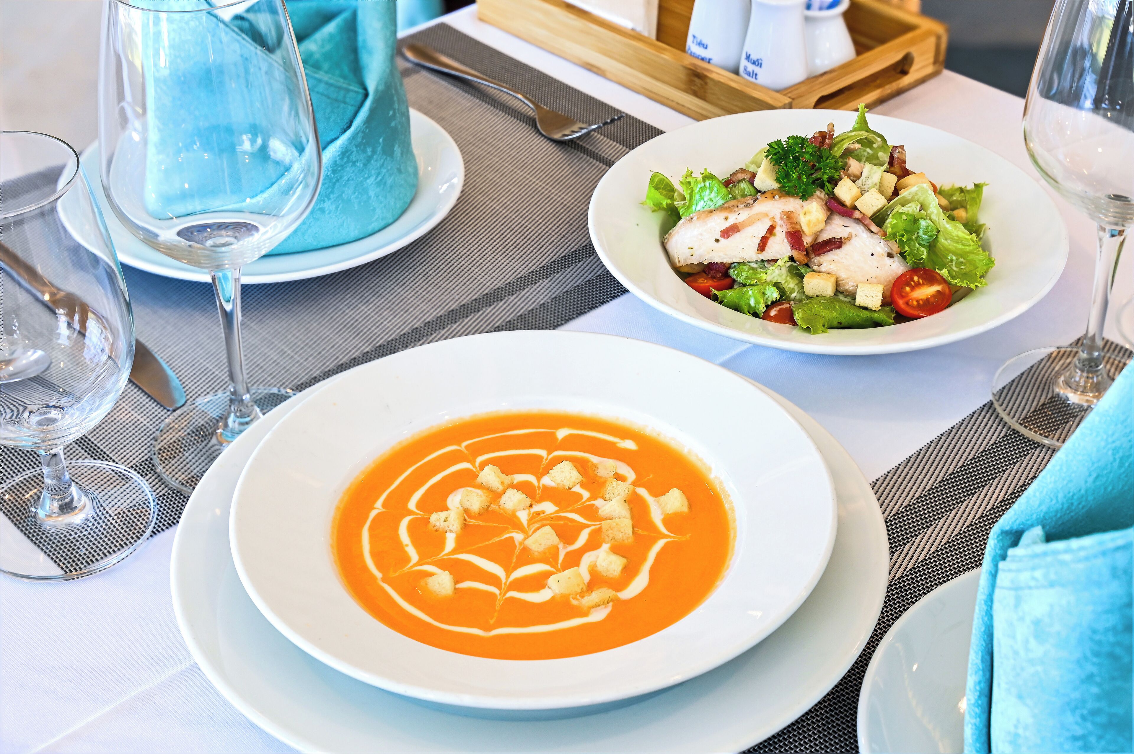 Een gedekte tafel met een kom soep, een salade en een glas wijn.