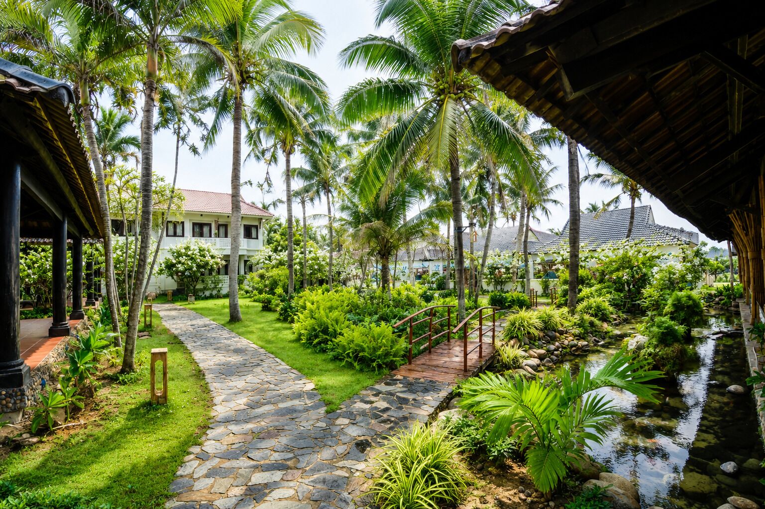 A tropical resort with a stone pathway leading to a house, surrounded by lush greenery and palm trees.