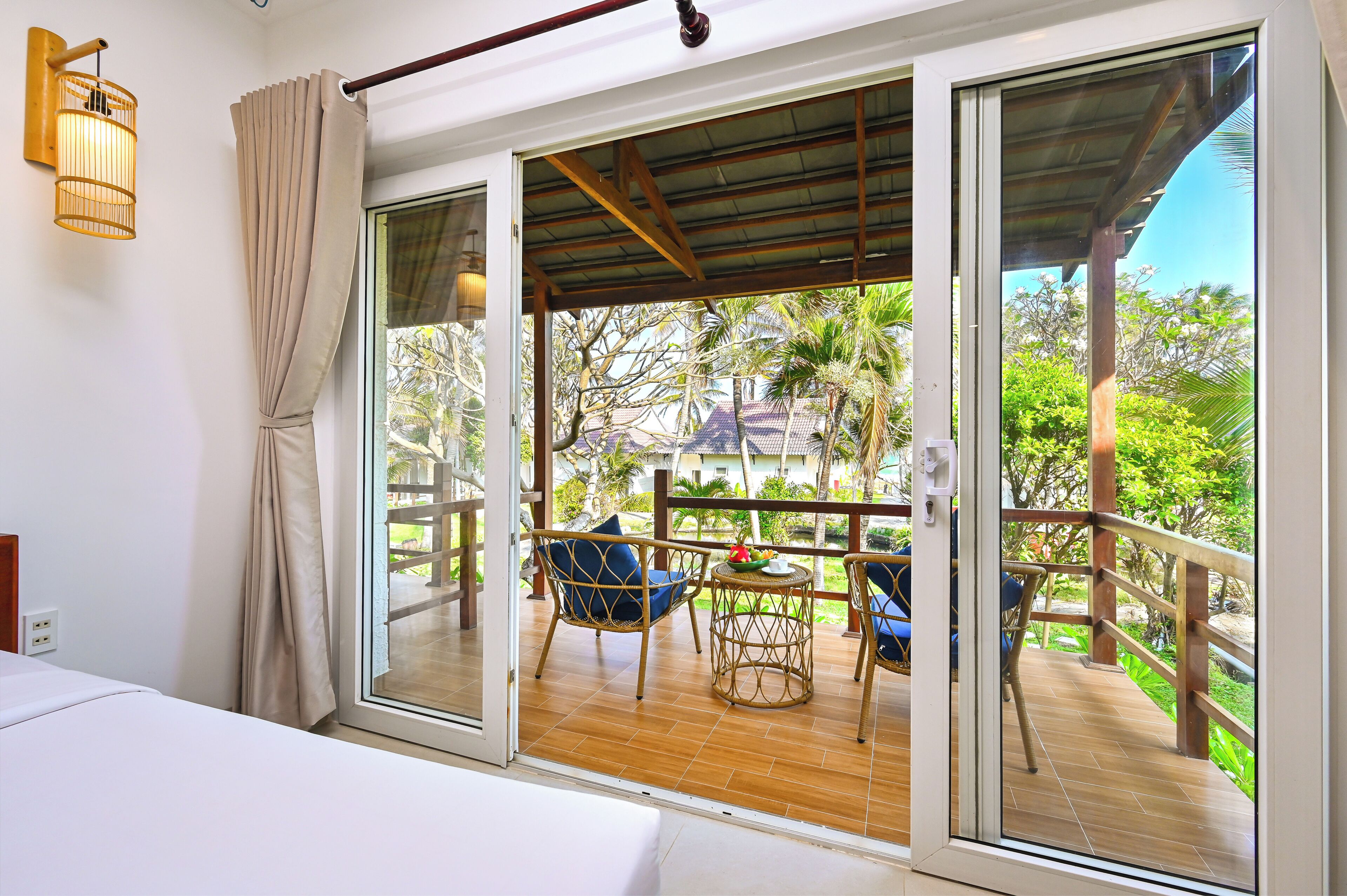 Una habitación con puerta corrediza de vidrio que da a un balcón con mobiliario de mimbre y vistas a zonas verdes.