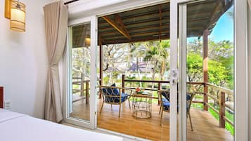 Una habitación con puerta corrediza de vidrio que da a un balcón con mobiliario de mimbre y vistas a zonas verdes.