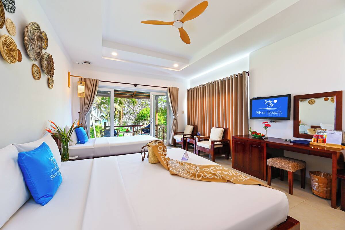 A hotel room with a bed, a desk with a television, and a view of the outdoors.