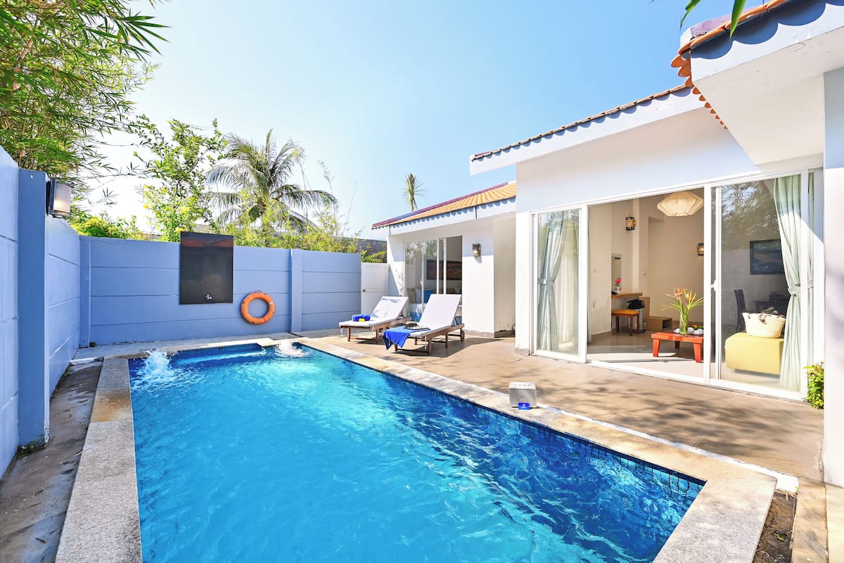 A swimming pool with lounge chairs, a lifebuoy, and a modern house with large windows and a patio.