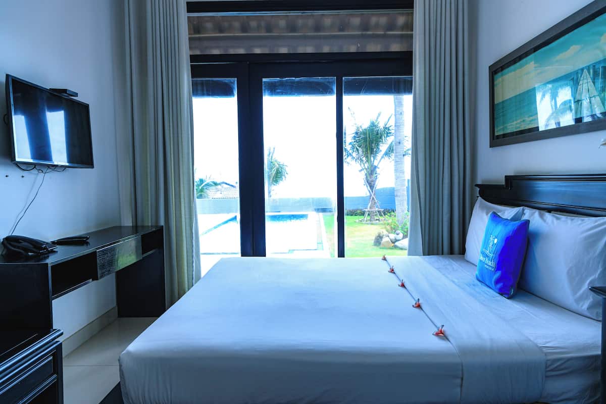A hotel room with a bed, a desk with a telephone, a television, and a view of the outdoors through a glass door.