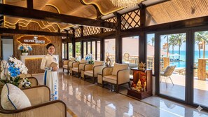 A reception area with a receptionist, wicker furniture, a reception desk, and a view of the pool and beach. - Silver Beach Resort Ke Ga (Tan Thanh)