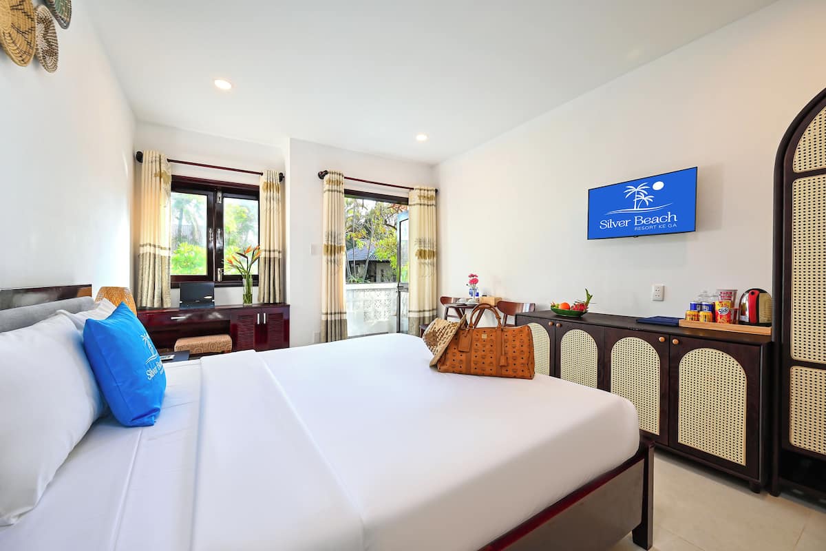 A hotel room with a bed, a TV, a desk, and a view of the outdoors.