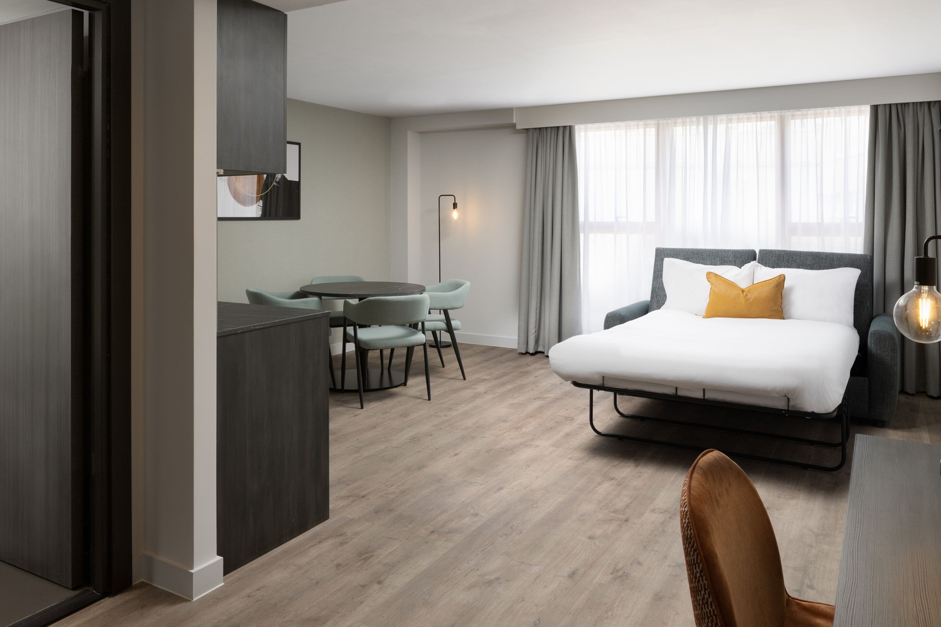 A modern hotel room with a bed, a desk, and a dining area.