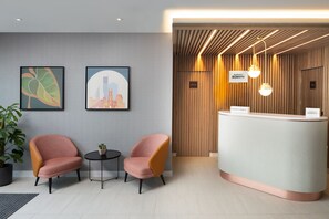 A reception area with a curved desk, two armchairs, a small table with a plant, and framed artwork on the wall. - Residence Inn by Marriott Manchester Piccadilly (Manchester)