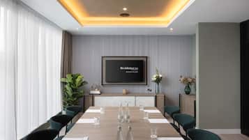 A modern conference room with a long table, chairs, a TV screen, and decorative plants.