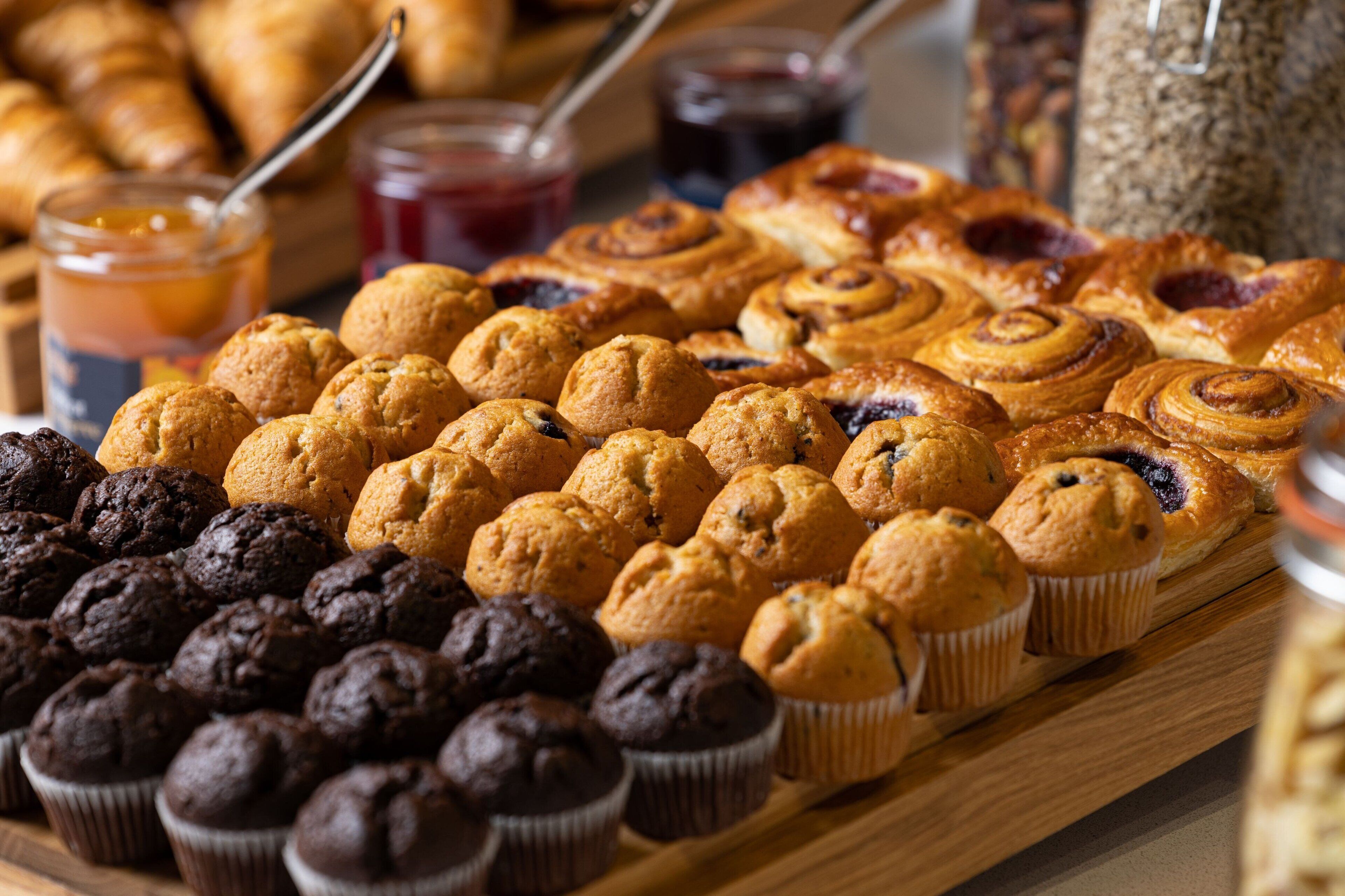 Különféle sütemények – például muffinok, croissant-ok és más tészták – egy fából készült tálcán.