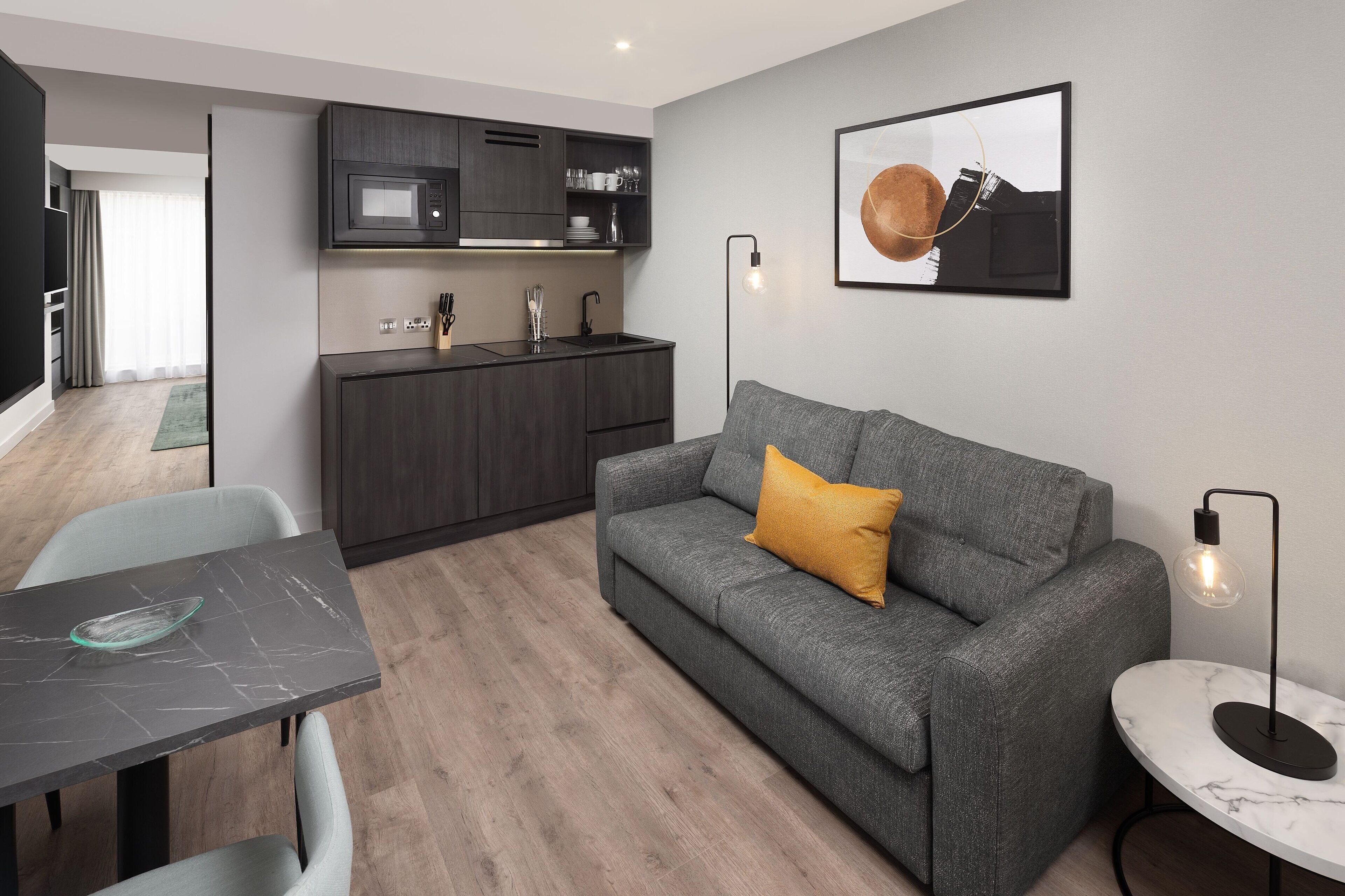 A modern living room with a grey sofa, a small table, and a kitchen area in the background.