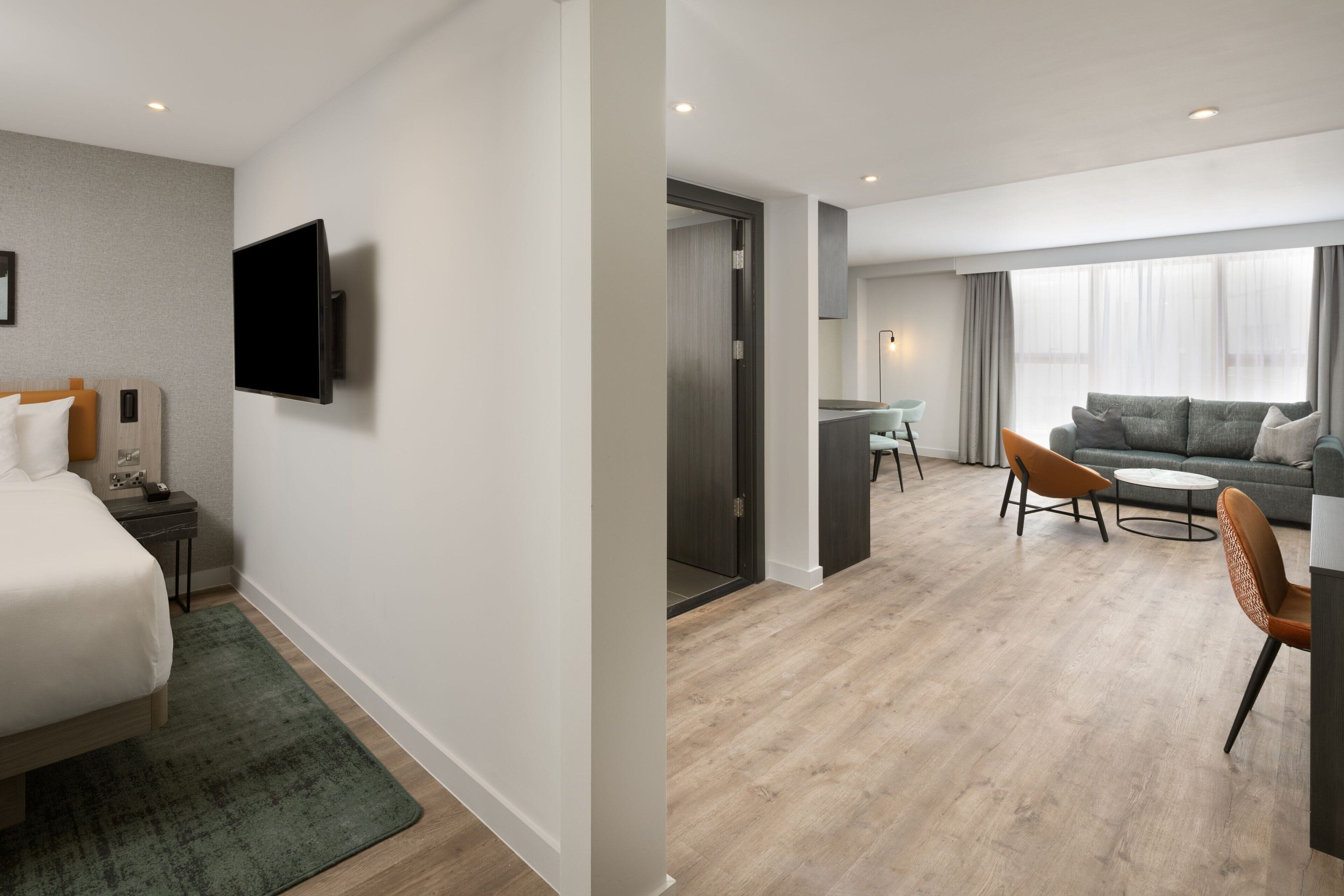 A modern hotel room with a bed, a flat-screen TV, a desk, and a sofa.