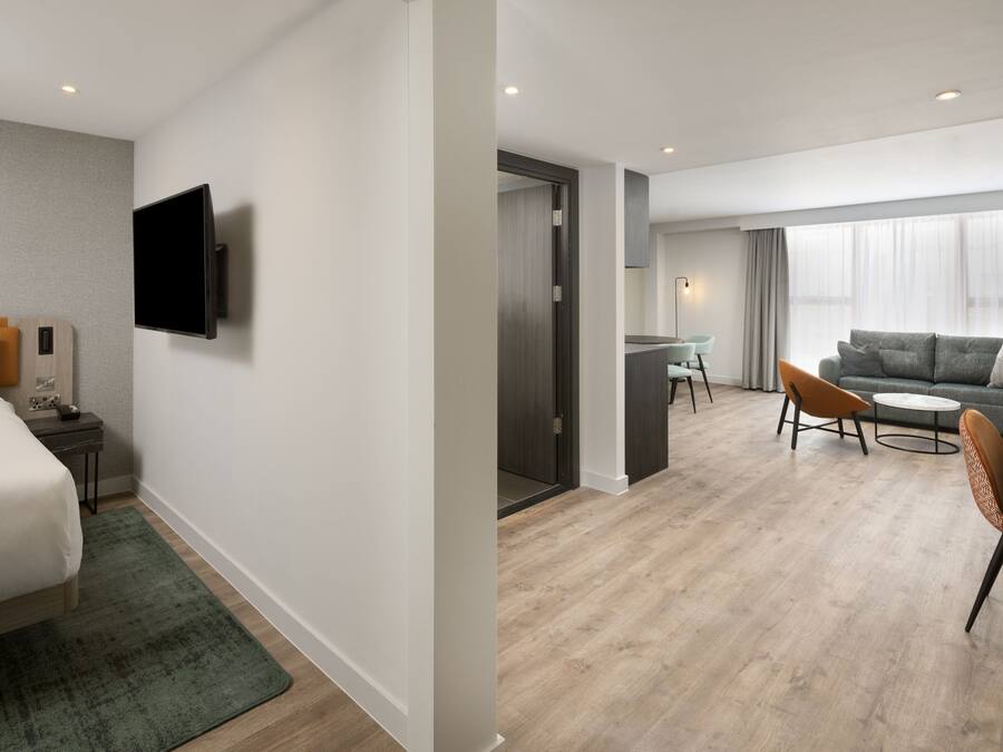 A modern hotel room with a bed, a flat-screen TV, a desk, and a sofa.