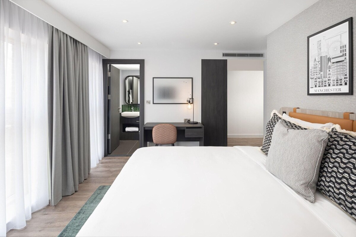 A hotel room with a large bed, a desk, a chair, and a bathroom visible through an open door.