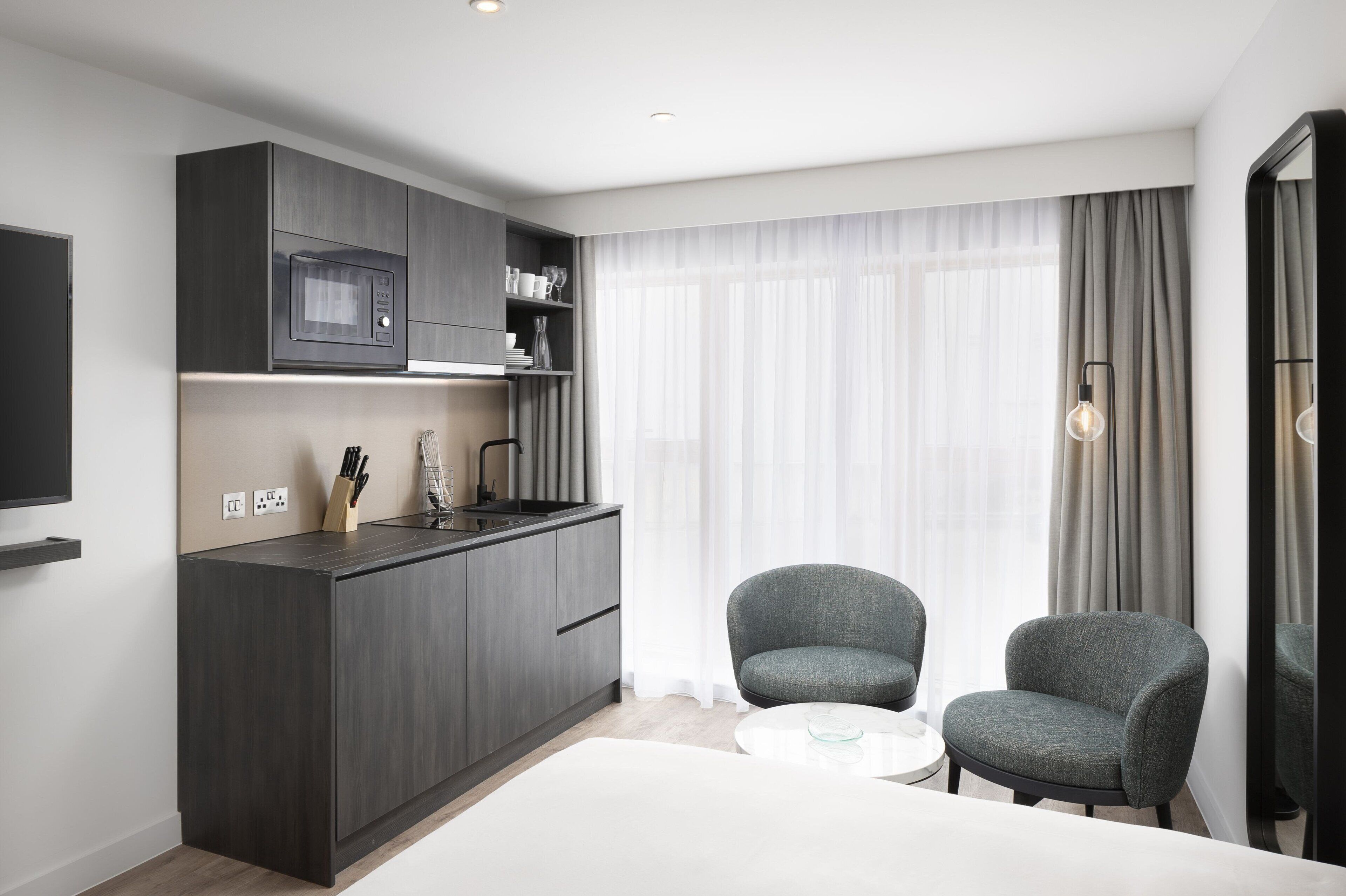 A modern kitchen with dark cabinetry, a microwave, and a small dining area with two chairs and a table.